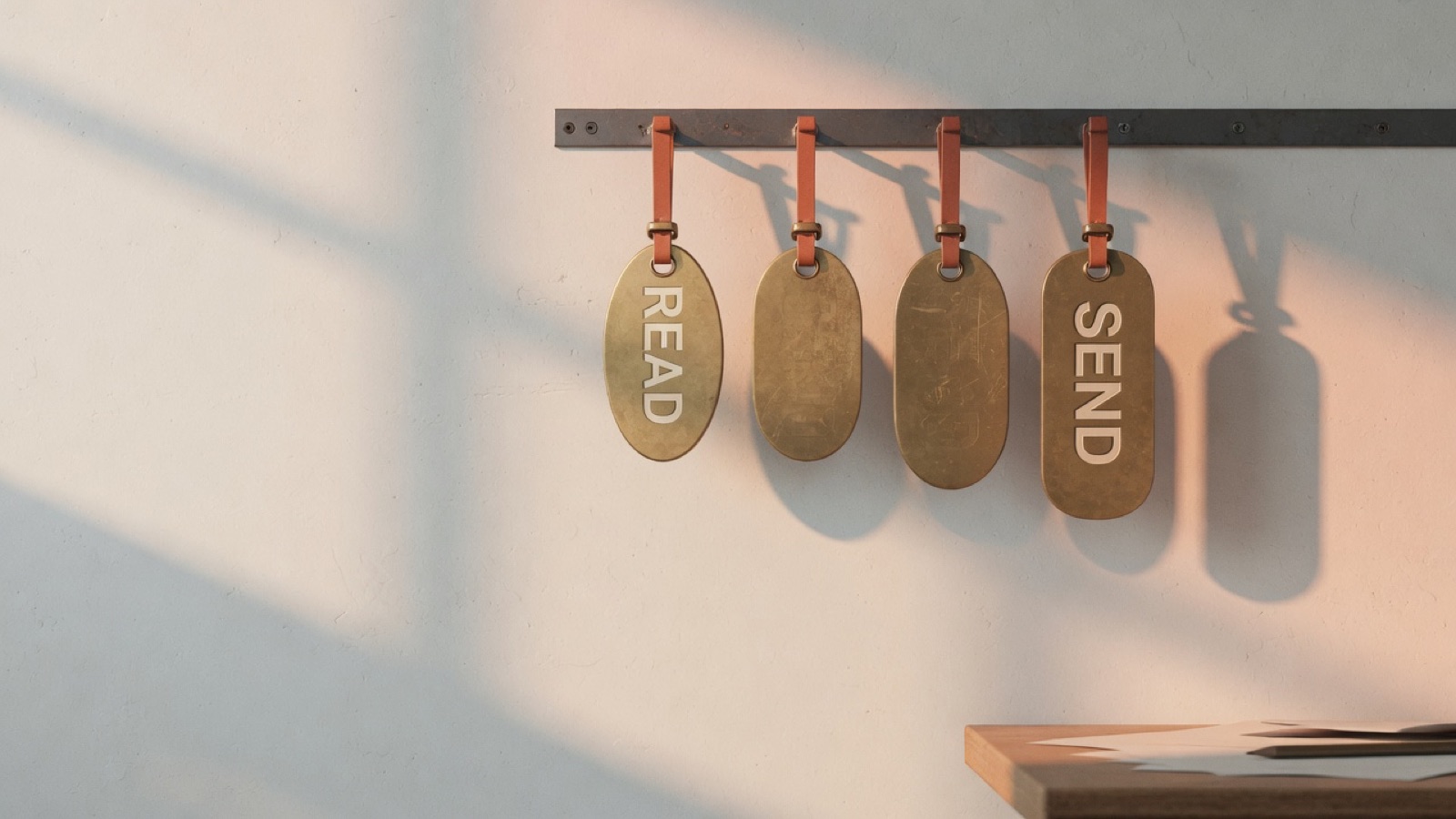 Four brass tags hanging from a steel rail against a sunlit wall, the first stamped READ and the last stamped SEND, the two between them worn blank.