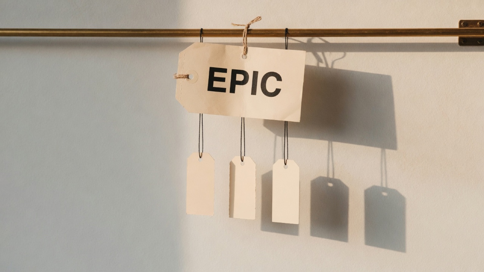 A single large paper tag hanging from a rail stamped EPIC, with three smaller blank tags suspended in a row beneath it on finer threads.