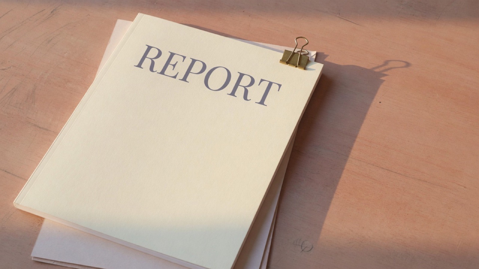 A neatly bound report with a ribbon beside a phone, a cup of tea and reading glasses.